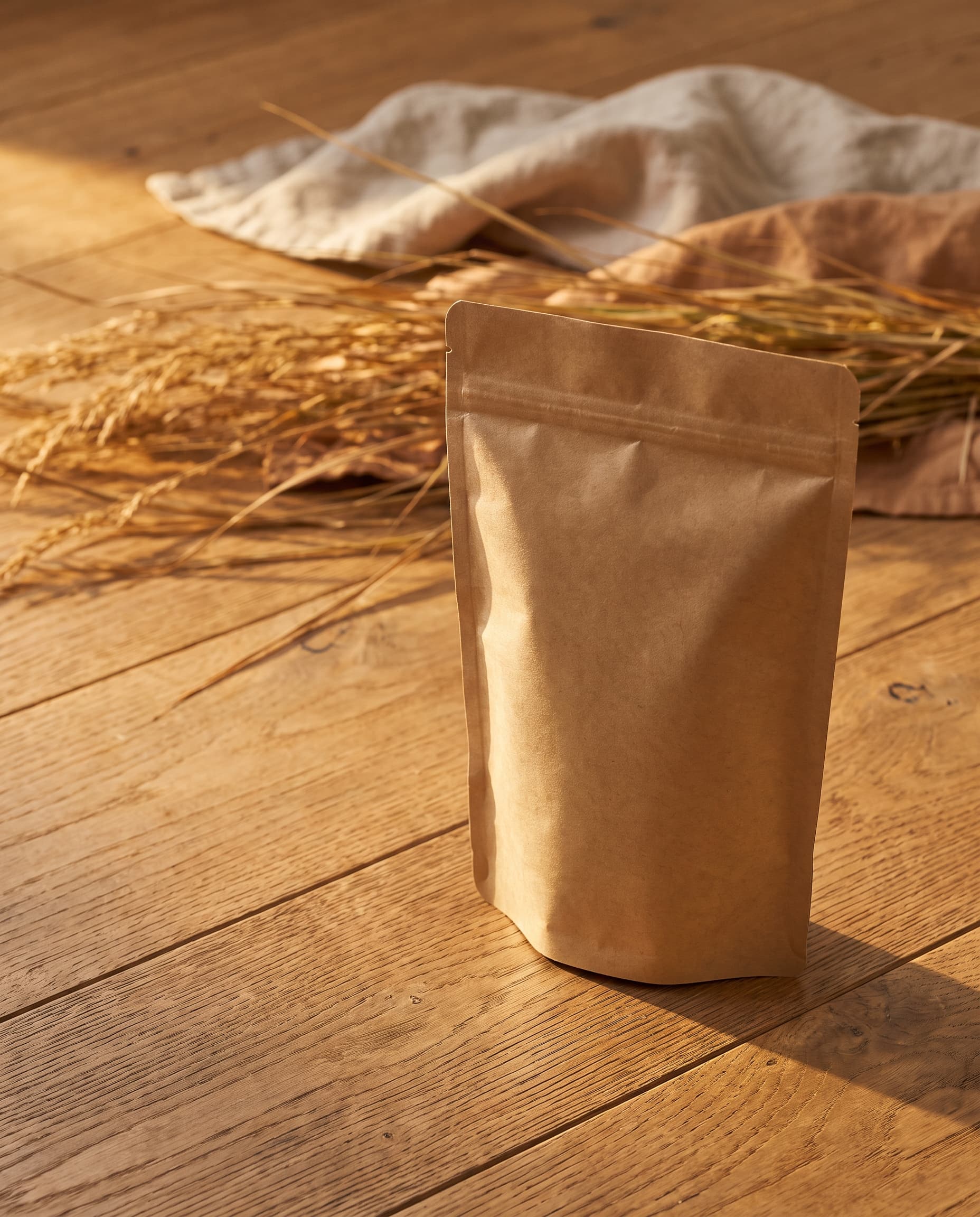 Unbranded kraft paper bag on warm oak with dried grasses and soft autumn light