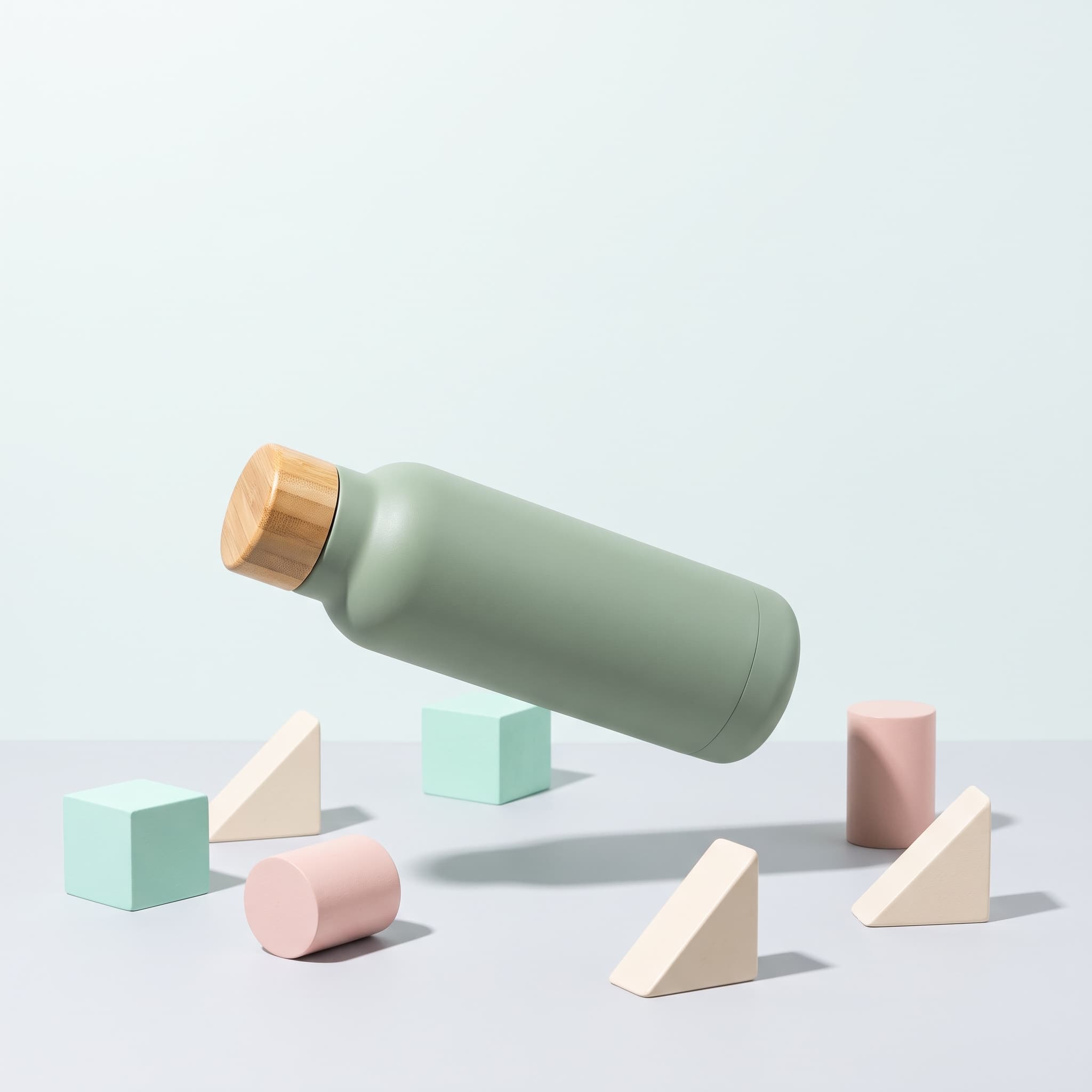 Unbranded sage water bottle floating above simple pastel geometric shapes