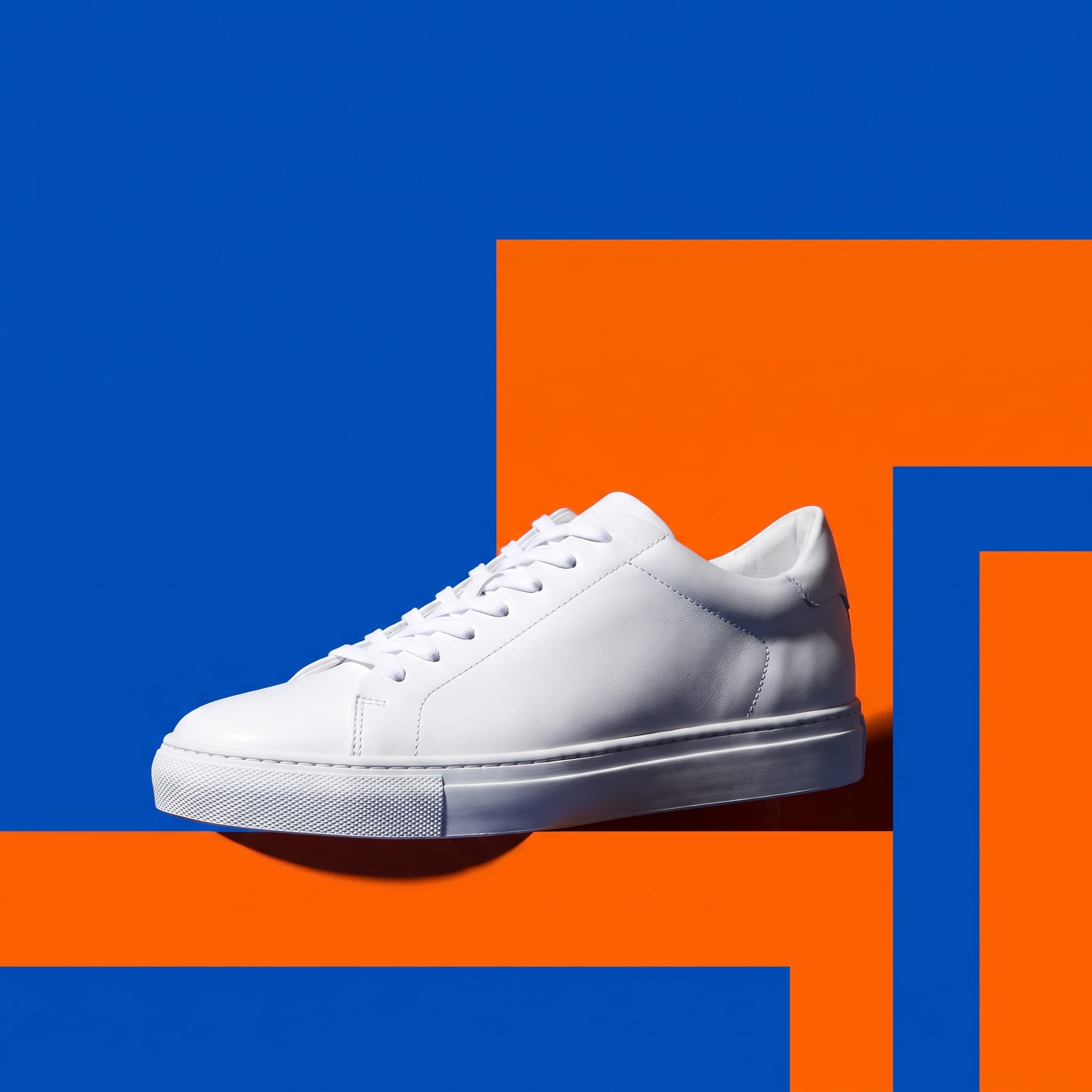 Plain white sneaker against bold cobalt and tangerine colour blocking with an empty corner