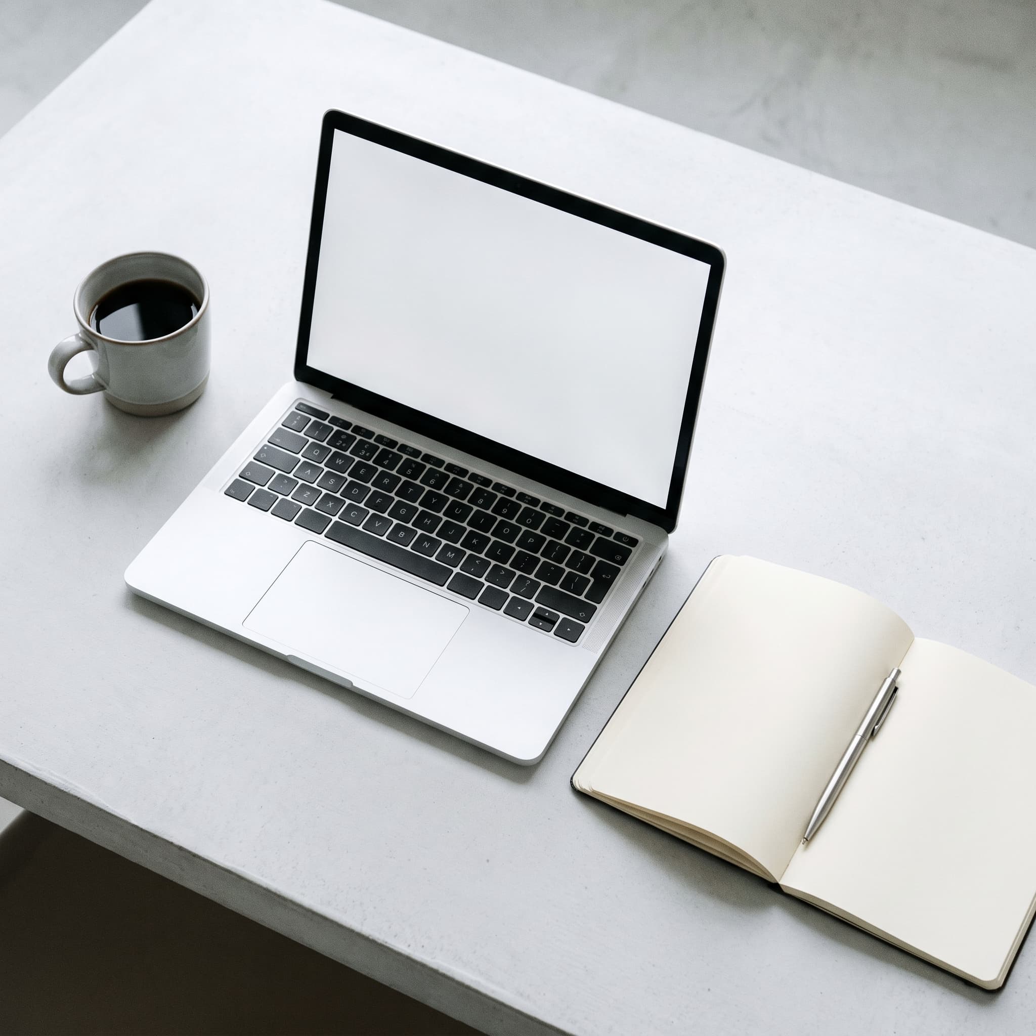 Overhead view of a tidy desk with a laptop, notebook and coffee cup