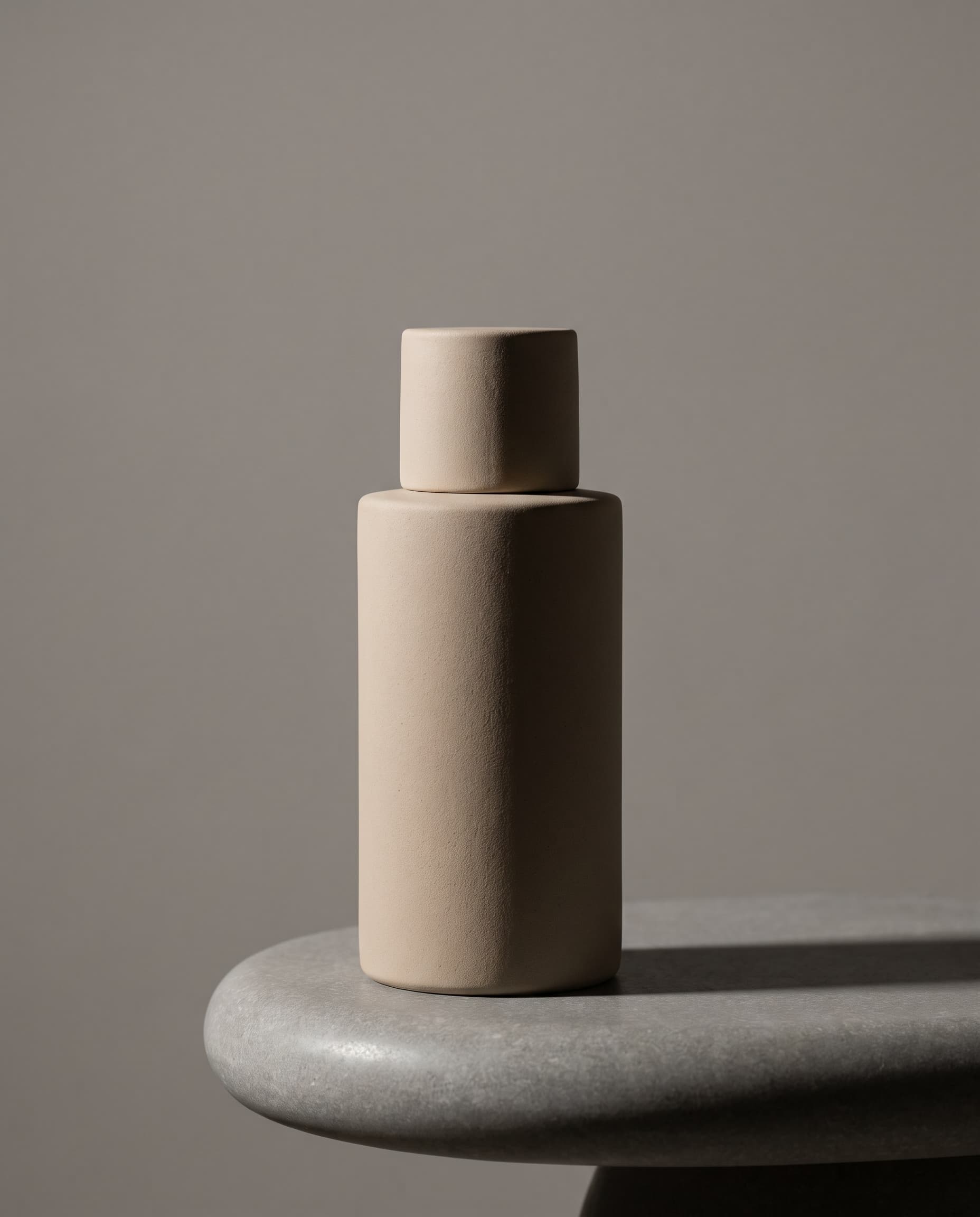 Unbranded ceramic skincare bottle standing on a smooth stone plinth in studio light