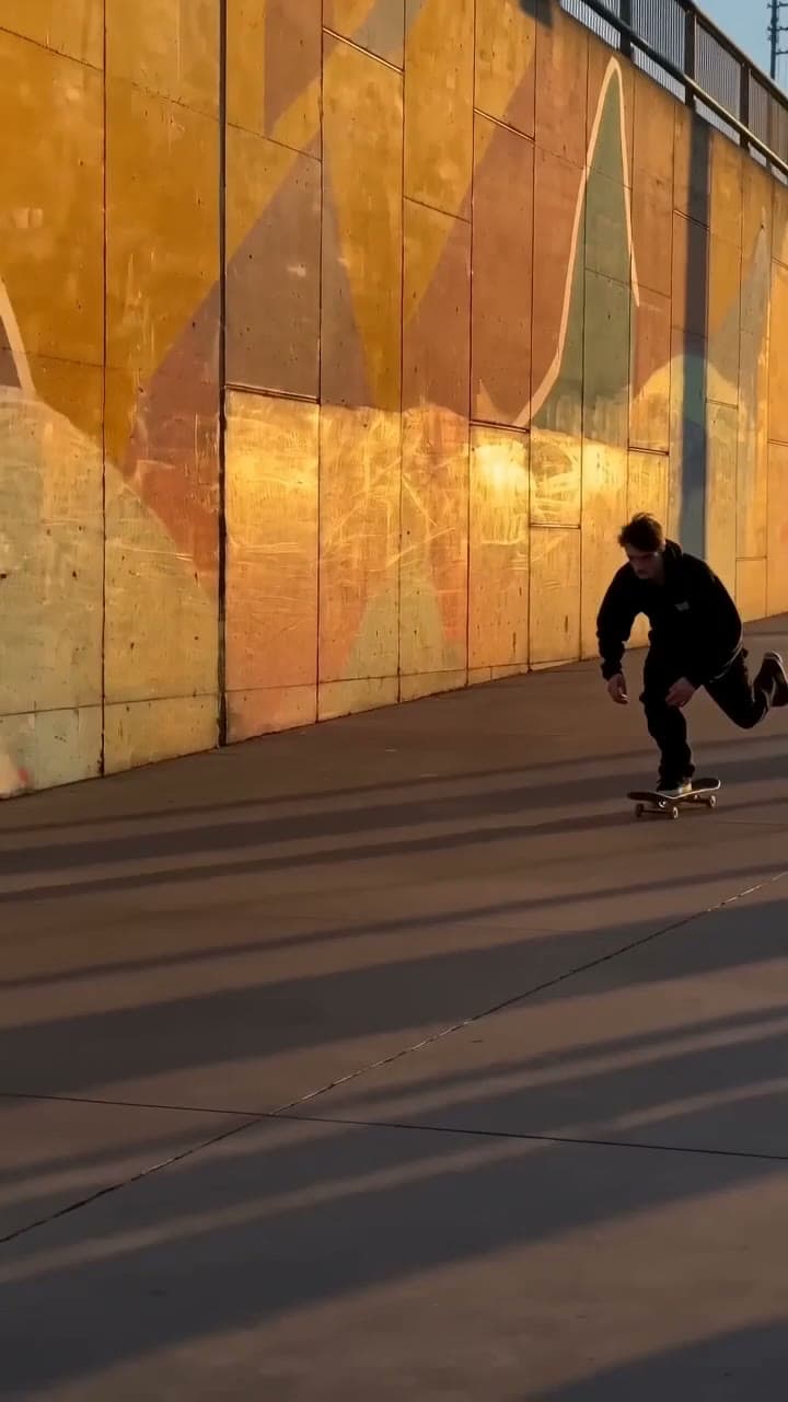 Vertical video of a skateboarder rolling into frame and landing a trick beside a painted wall