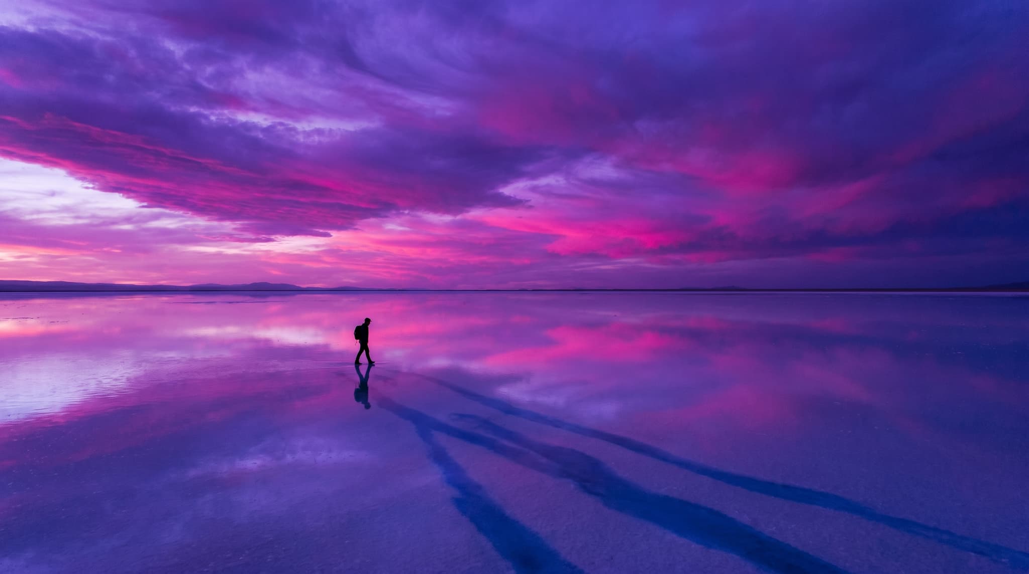 A lone figure crossing a mirrored salt flat beneath a violet sky