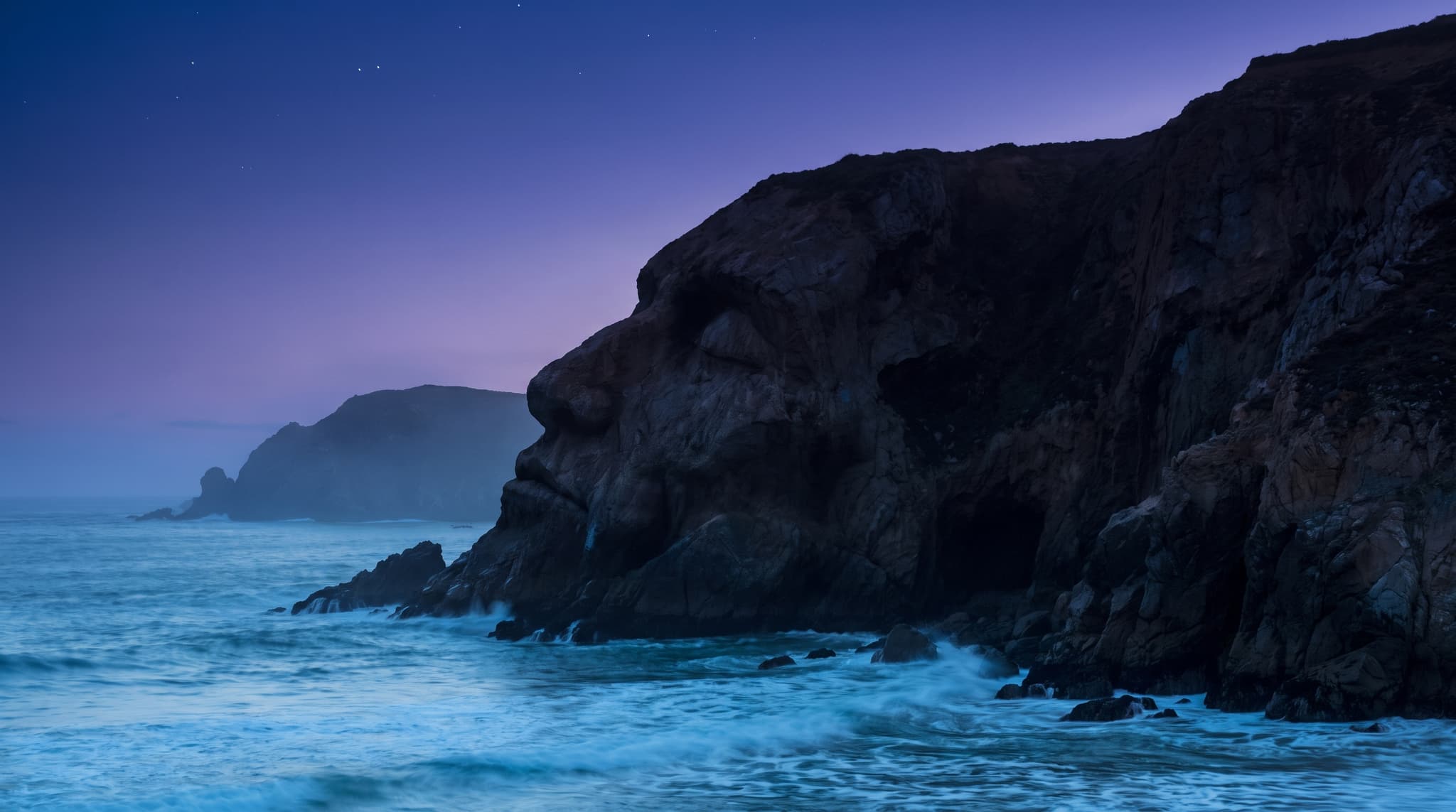 A coastal cliff at dusk whose rock face also reads as a sleeping profile