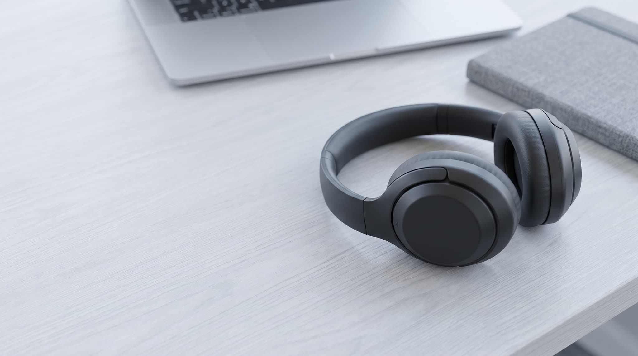 Unbranded over-ear headphones on a tidy desk with a laptop softly out of focus behind