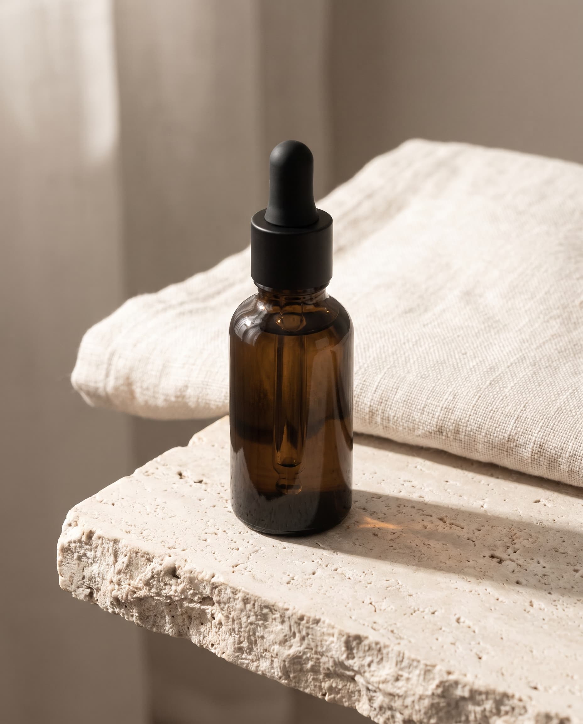 Unbranded amber glass serum bottle on a travertine ledge in soft morning light
