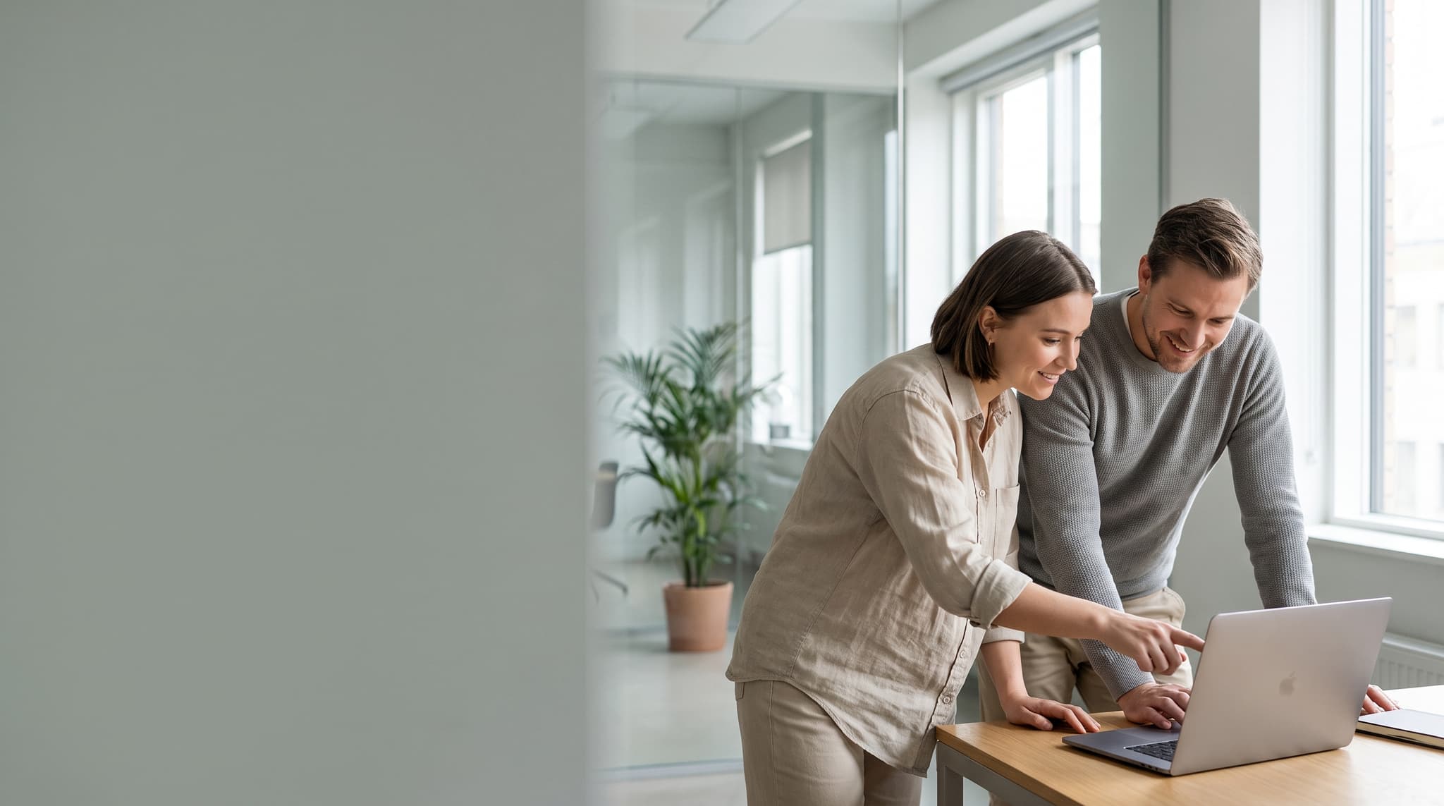 Two colleagues reviewing work on a laptop beside a large office window
