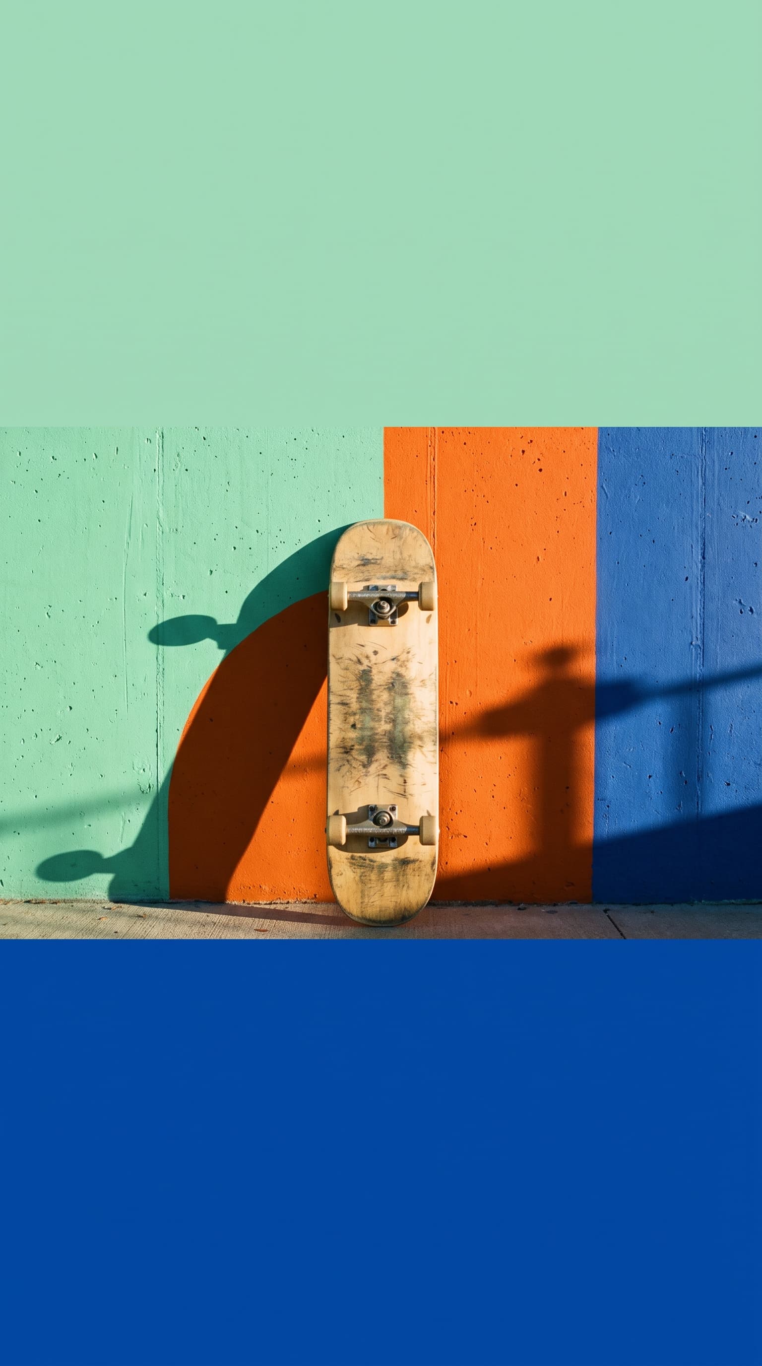 A skateboard leaning against a painted concrete wall casting a long golden-hour shadow